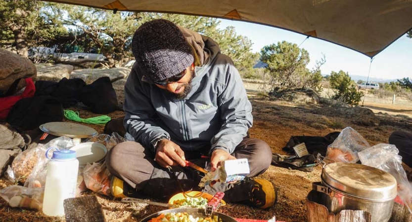 A person prepares food under a tarp shelter